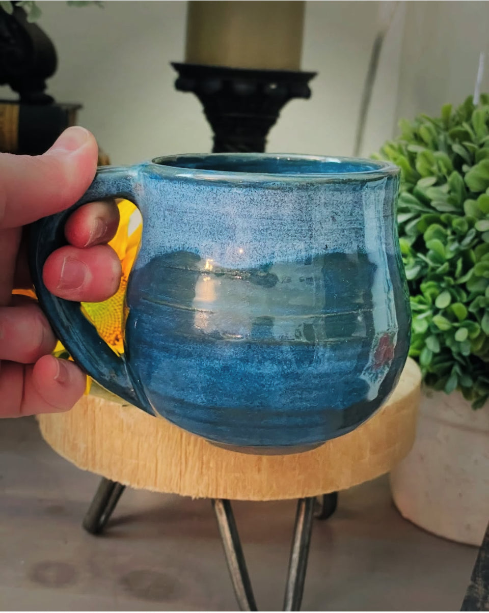 Side view of artisan blue stoneware coffee mug with greenery